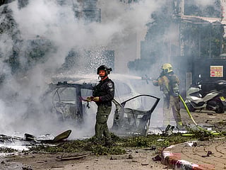 An Israeli policeman looks on as behind a firefighter extinguishes a blaze in a vehicle following a projectile impact from an Iranian strike in southern Tel Aviv on March 15, 2026.  
