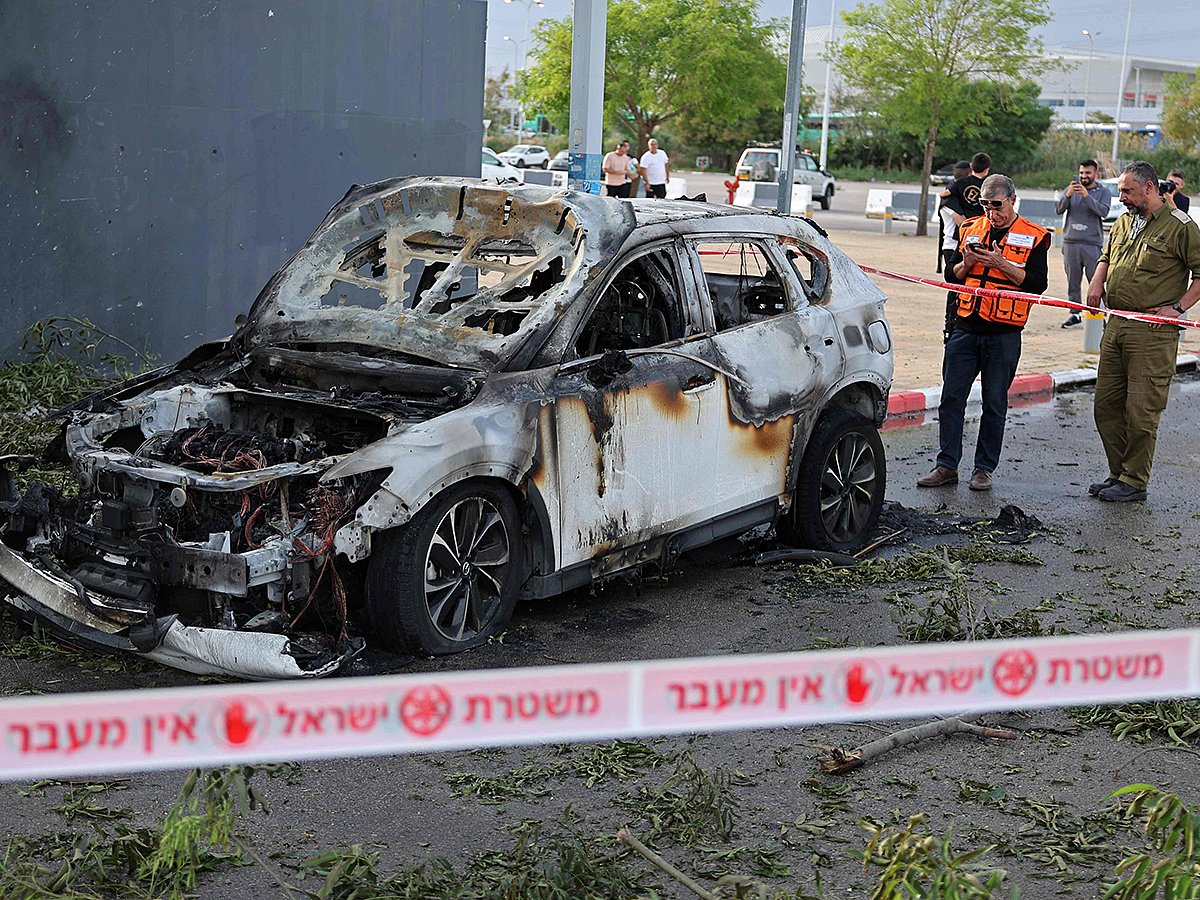 An Israeli security personnel and a first responder inspect the site of an Iranian strike that hit a car in Petah Tikva on March 18, 2026. 