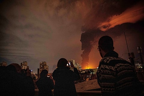 Residents watch and take pictures as flames and smoke rise from an oil storage facility struck as attacks hit the city during the US–Israeli military campaign in Tehran, Iran, Saturday, March 7, 2026. (Alireza Sotakbar/ISNA via AP)