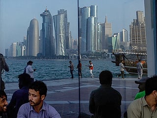 People sit with the reflection of the Doha skyline along the Doha Corniche. 