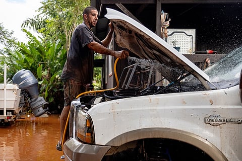 Philip Holman flushes mud from his lifted truck's engine bay the day after it was fully submerged by the fast-moving flood in Haleiwa, Hawaii Saturday, March 21, 2026. (Stephen Lam/San Francisco Chronicle via AP)