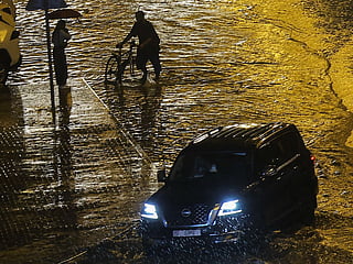 Vehicles and pedestrians struggle to pass a waterlogged street in Sharjah amid persistent rainfall on Friday.  