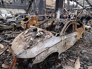 Iranian officials and journalists stand next to the wreckage of vehicles during the visit of a car service centre in eastern Tehran that was hit by a missile strike, on March 28, 2026. 
