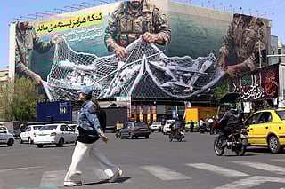 Commuters make their way past a billboard with a sentence reading ‘The Strait of Hormuz remains closed’ at the Enqelab Square in Tehran, on April 5, 2026.