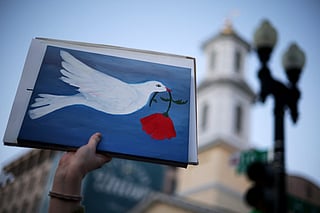 An Anti-war demonstrator holds up a sign with a symbol of peace as they gather near the White House to protest the war in Iran on April 7, 2026 in Washington, DC. 