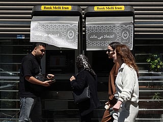 People walk past an ATM machine installed along a street in Tehran on April 15, 2026. 