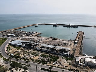 Backdropped by ships in the Strait of Hormuz, damage, according to local witnesses caused by several recent airstrikes, is seen on a fishing pier in the port of Qeshm island, Iran. 