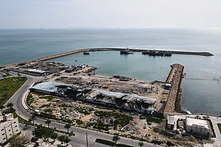 Backdropped by ships in the Strait of Hormuz, damage, according to local witnesses caused by several airstrikes during the US-Israel military campaign in April, is seen on a fishing pier in the port of Qeshm island, Iran.