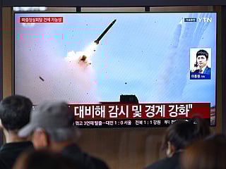 People watch a television screen showing a news broadcast with file footage of a North Korean missile test, at a train station in Seoul on April 19, 2026.