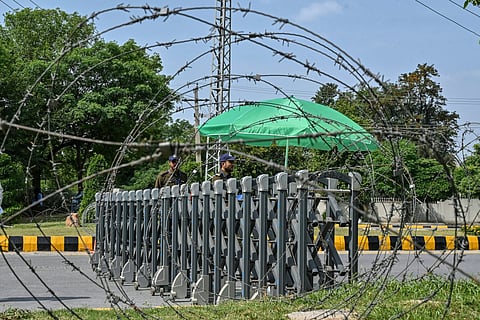 Security personnel keeping watch are seen through barbed wires at a closed road leading to the Serena Hotel in the Red Zone area of Islamabad on April 23, 2026.