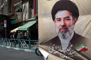 Iranians stand on a pavement along a street next to a billboard depicting Iran's Supreme Leader Ayatollah Mojtaba Khamenei, in Tehran on April 24, 2026.