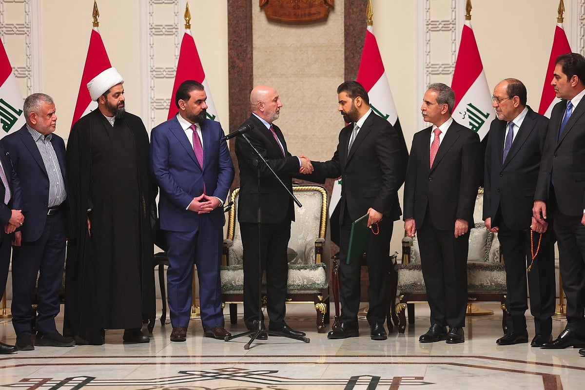 This handout photograph taken and released by the Iraqi Presidency Press Office on April 27, 2026 shows Iraq's President Nizar Amede (4th L) shaking hands with newly Iraq's Prime Minister designated Ali al-Zaidi (4th R), surrounded by Iraqi political leaders, at the Presidential Palace in Bagdad.