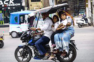 A commuter rides a two-wheeler with his family and shields it to protect them from the scorching heat in Hyderabad on April 24, 2026.