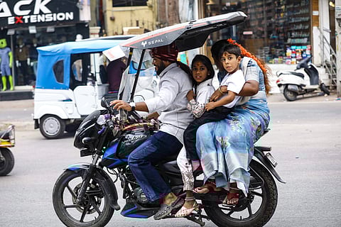 A commuter rides a two-wheeler with his family and shields it to protect them from the scorching heat in Hyderabad on April 24, 2026.
