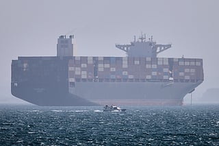 A container ship sits at anchor as a small motorboat passes in the foreground in the Strait of Hormuz off Bandar Abbas, Iran, on Saturday, May 2, 2026. 