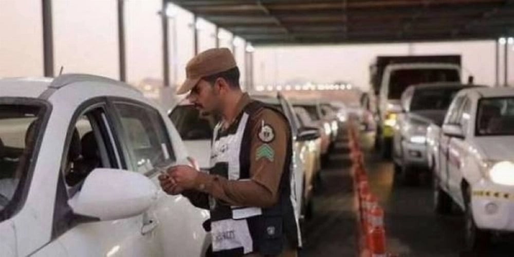 Saudi police man verifies ID documents and Hajj permits at a checkpoint.  