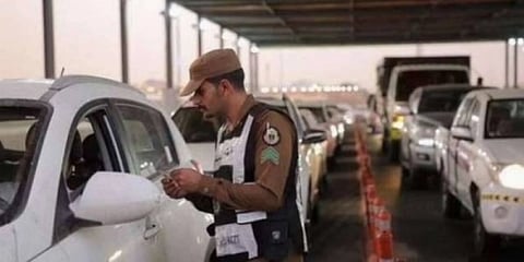 Saudi police man verifies ID documents and Hajj permits at a checkpoint.  