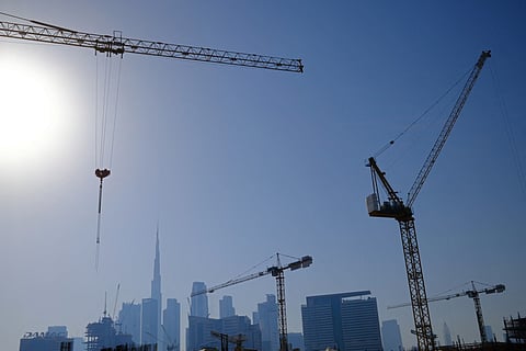 Cranes at a construction site are silhouetted against Burj Khalifa, the world’s tallest building and the Dubai skyline, on May 13, 2026.