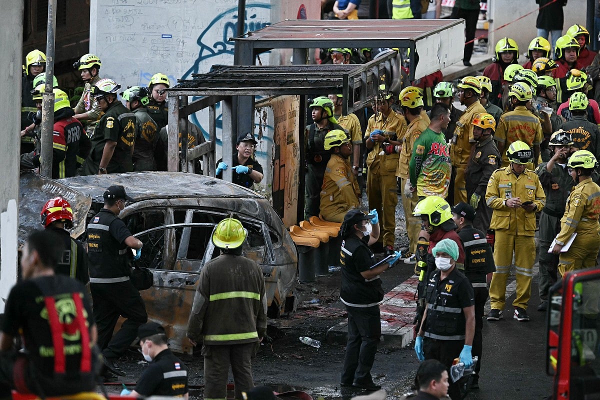 Forensic police officers, rescue workers and firefighters stand at the site of a train collision with a bus underneath Makkasan Airport Rail station in Bangkok on May 16, 2026.
