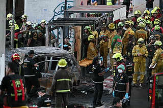 Forensic police officers, rescue workers and firefighters stand at the site of a train collision with a bus underneath Makkasan Airport Rail station in Bangkok on May 16, 2026.