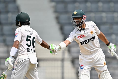 Pakistan’s captain Shan Masood (R) celebrates with teammate Babar Azam (L) after scoring a half-century (50 runs) during the fourth day of the second Test cricket match between Bangladesh and Pakistan at the Sylhet International Cricket Stadium in Sylhet on May 19, 2026.
