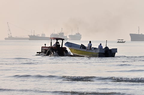 A tractor tows a small boat through shallow water as cargo ships and industrial vessels are anchored in the Strait of Hormuz off Bandar Abbas, Iran, Monday, June 1, 2026.  