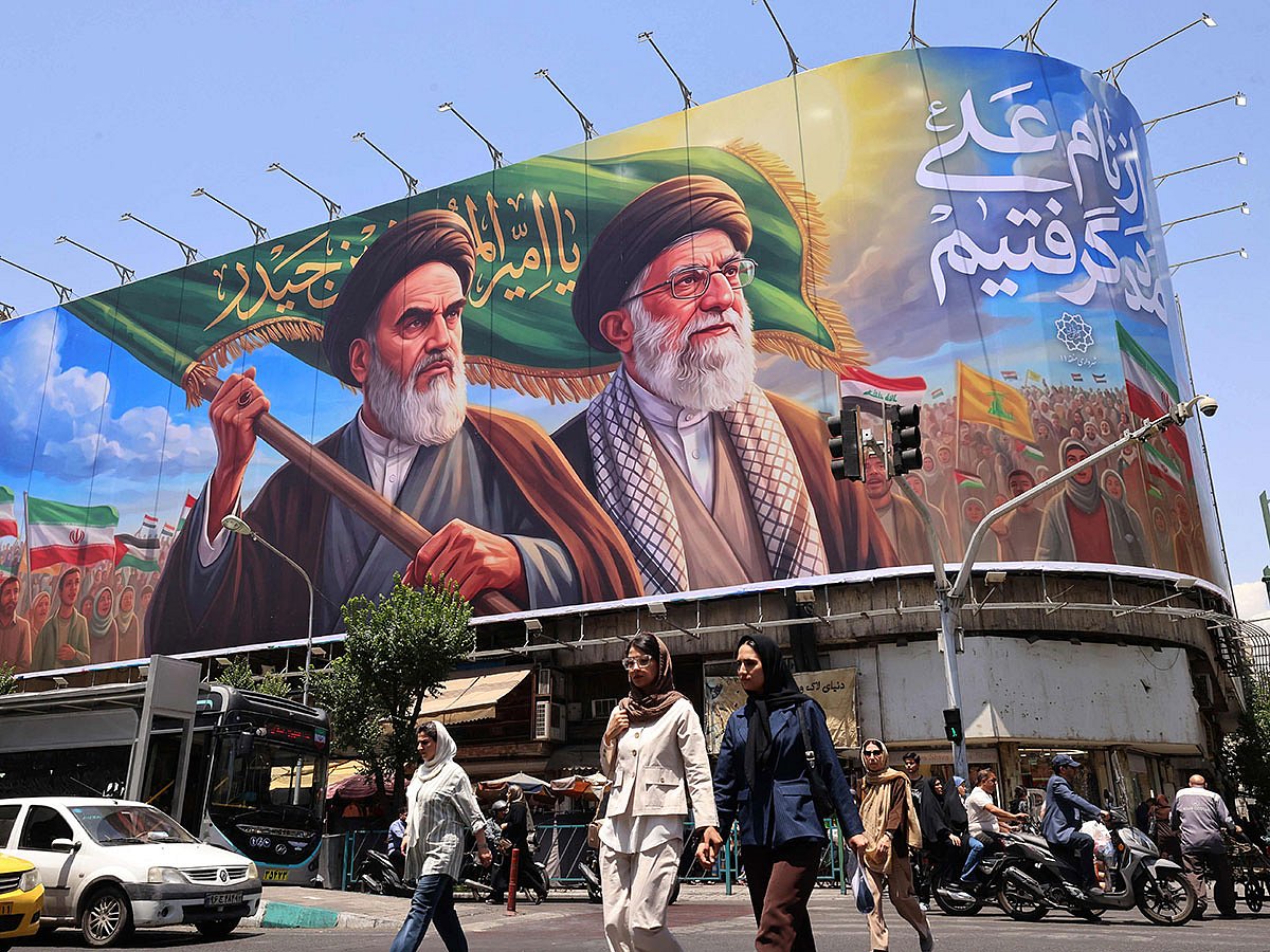 People cross the street past a large billboard showing portraits of Iran's late supreme leader, Ayatollah Ruhollah Khomeini (L) and slain supreme leader Ayatollah Ali Khamenei (R) in central Tehran