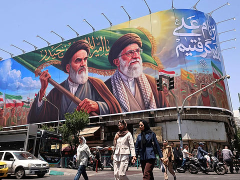 People cross the street past a large billboard showing portraits of Iran's late supreme leader, Ayatollah Ruhollah Khomeini (L) and slain supreme leader Ayatollah Ali Khamenei (R) in central Tehran