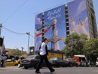 A woman walks past a giant banner depicting Iranian missiles and a sword belonging to Imam Ali, the first Imam of the Shiites, at the Vanak Square in Tehran. 