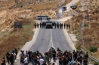 Protesters and local Palestinian landowners, who say some of their land was taken for the newly built Mount Tarousa settlement (background), run from tear gas fired by Israeli security forces blocking a road leading to the hilltop during a rally against the settlement near Dura in the Israeli-occupied West Bank on June 19, 2026.