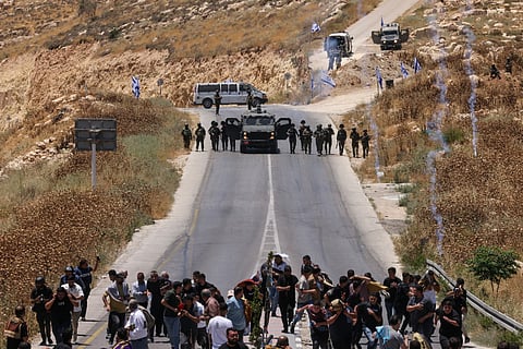 Protesters and local Palestinian landowners, who say some of their land was taken for the newly built Mount Tarousa settlement (background), run from tear gas fired by Israeli security forces blocking a road leading to the hilltop during a rally against the settlement near Dura in the Israeli-occupied West Bank on June 19, 2026.