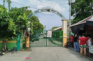 People stand next to the entrance gate of San Jose National High School after a shooting incident in Tacloban City, Leyte province on June 22, 2026.