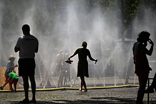 People stand near over water hoses spilling water to provide relief from the summer heat as part of Cologne’s climate adaptation measures in Cologne, western Germany on June 25, 2026 during a heatwave in Europe.