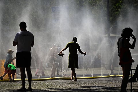 People stand near over water hoses spilling water to provide relief from the summer heat as part of Cologne’s climate adaptation measures in Cologne, western Germany on June 25, 2026 during a heatwave in Europe.