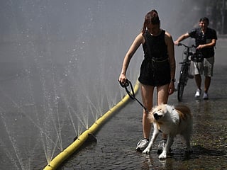 A woman walks her dog past water hoses spilling water to provide relief from the summer heat as part of Cologne’s climate adaptation measures in Cologne, western Germany on June 25, 2026 during a heatwave in Europe.