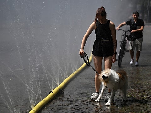 A woman walks her dog past water hoses spilling water to provide relief from the summer heat as part of Cologne’s climate adaptation measures in Cologne, western Germany on June 25, 2026 during a heatwave in Europe.