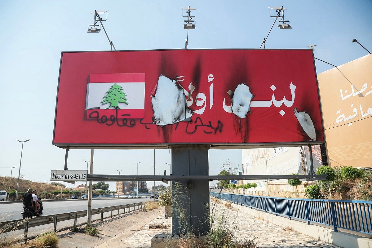 Vehicles drive past a billboard that reads in Arabic "Lebanon first" (in white) after it was defaced with the words "Army, People, Resistance" and set on fire along Beirut's airport road near Tehran-backed Hezbollah's stronghold, amidst tensions following Lebanon's framework agreement with Israel on June 28, 2026.
