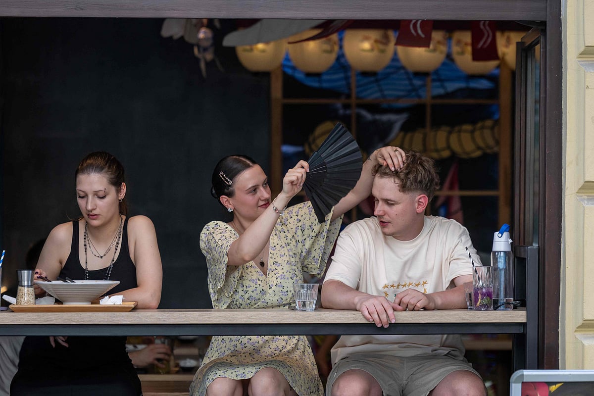 A girl cools a boy with her folding fan as they sit in a wide-open restaurant window in central Warsaw during the heatwave that has reached Polandon June 27, 2026.  