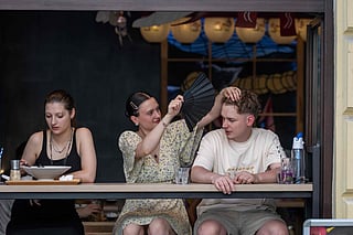 A girl cools a boy with her folding fan as they sit in a wide-open restaurant window in central Warsaw during the heatwave that has reached Polandon June 27, 2026.  