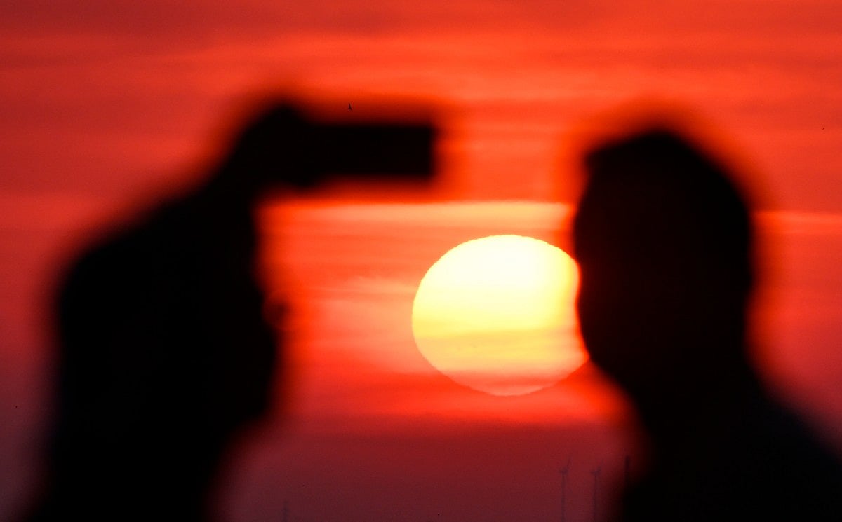A person takes a photo as the sun going up on early June 28, 2026, over the Drachenberg mountain in Berlin, as the German capital is expected to reach teperatures around 40 degrees Celsius during a heatwave in Europe.