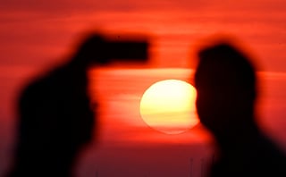 A person takes a photo as the sun going up on early June 28, 2026, over the Drachenberg mountain in Berlin, as the German capital is expected to reach teperatures around 40 degrees Celsius during a heatwave in Europe.