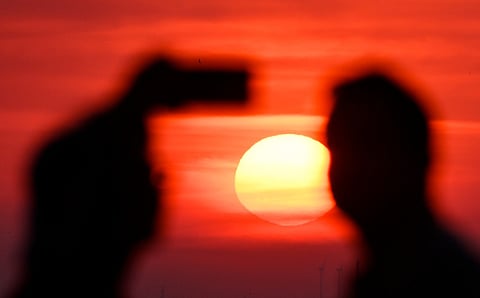 A person takes a photo as the sun going up on early June 28, 2026, over the Drachenberg mountain in Berlin, as the German capital is expected to reach teperatures around 40 degrees Celsius during a heatwave in Europe.