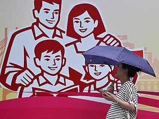 A woman holding an umbrella walking past a billboard of a happy family in Hanoi. 