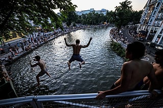 Youths jump from a bridge into the Canal Saint-Martin as France experiences a heatwave, in Paris on June 25, 2026.