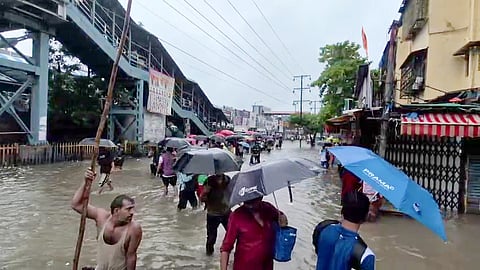 People carrying umbrellas wade through the waterlogged area caused by rain, in Mumbai on Sunday. (Photo: ANI Video Grab)