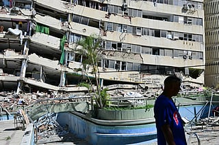 A man walks past a partially collapsed apartment building.