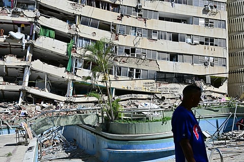 A man walks past a partially collapsed apartment building.