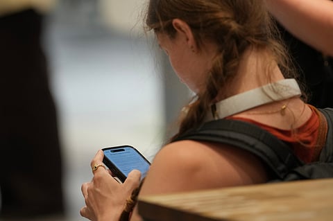A teenager looks at her mobile phone in London, Monday, June 15, 2026. 