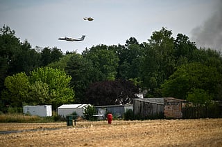This photograph shows a Dash 8-Q400MR aircraft of the civil security and a firefighter helicopter operating near a plume of smoke from a fire in the Fontainebleau Forest, in Noisy-sur-Ecole, in the Paris' Ile-de-France region on July 16, 2026.