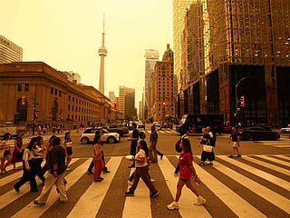 People walk in downtown Toronto, as smoke from forest fires in Northern Ontario causes poor air quality over the city, in Toronto, Ontario, Canada, July 15, 2026.  